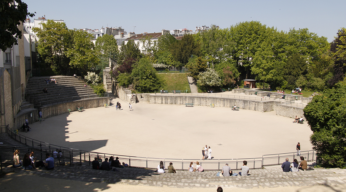 people sat around a huge sandy arena surrounded by trees
